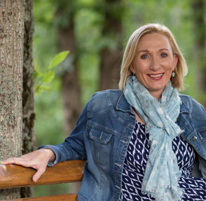 Image of author headshot of Carrie Cox seated on a bench smiling