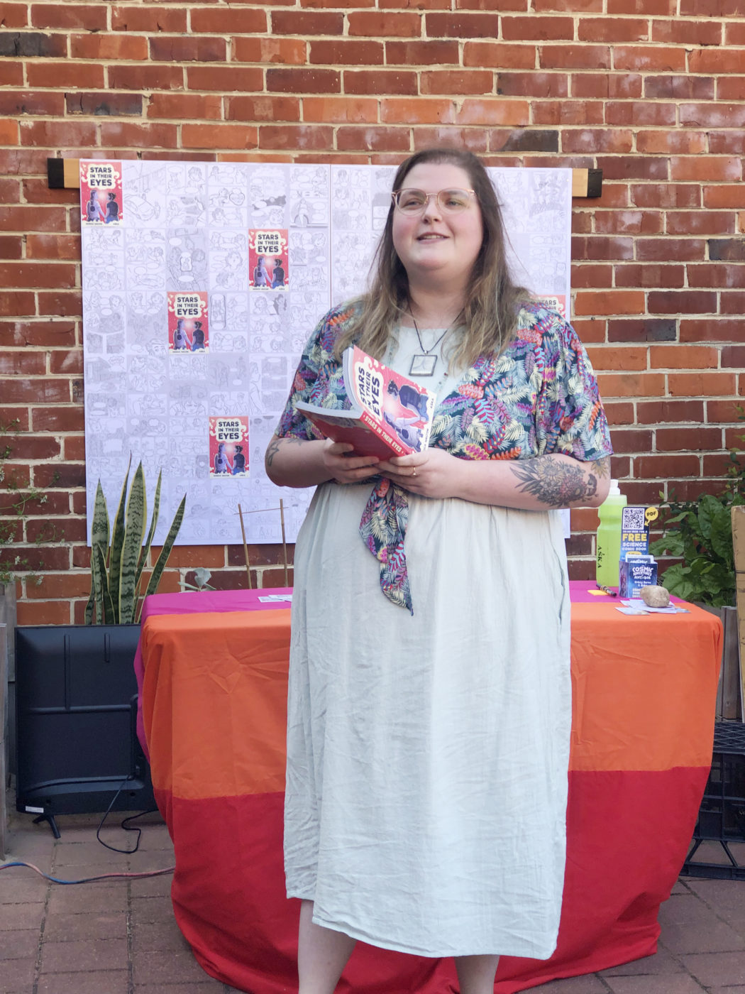 Image of a woman in a white dress standing in front of a table holding a book in front of her
