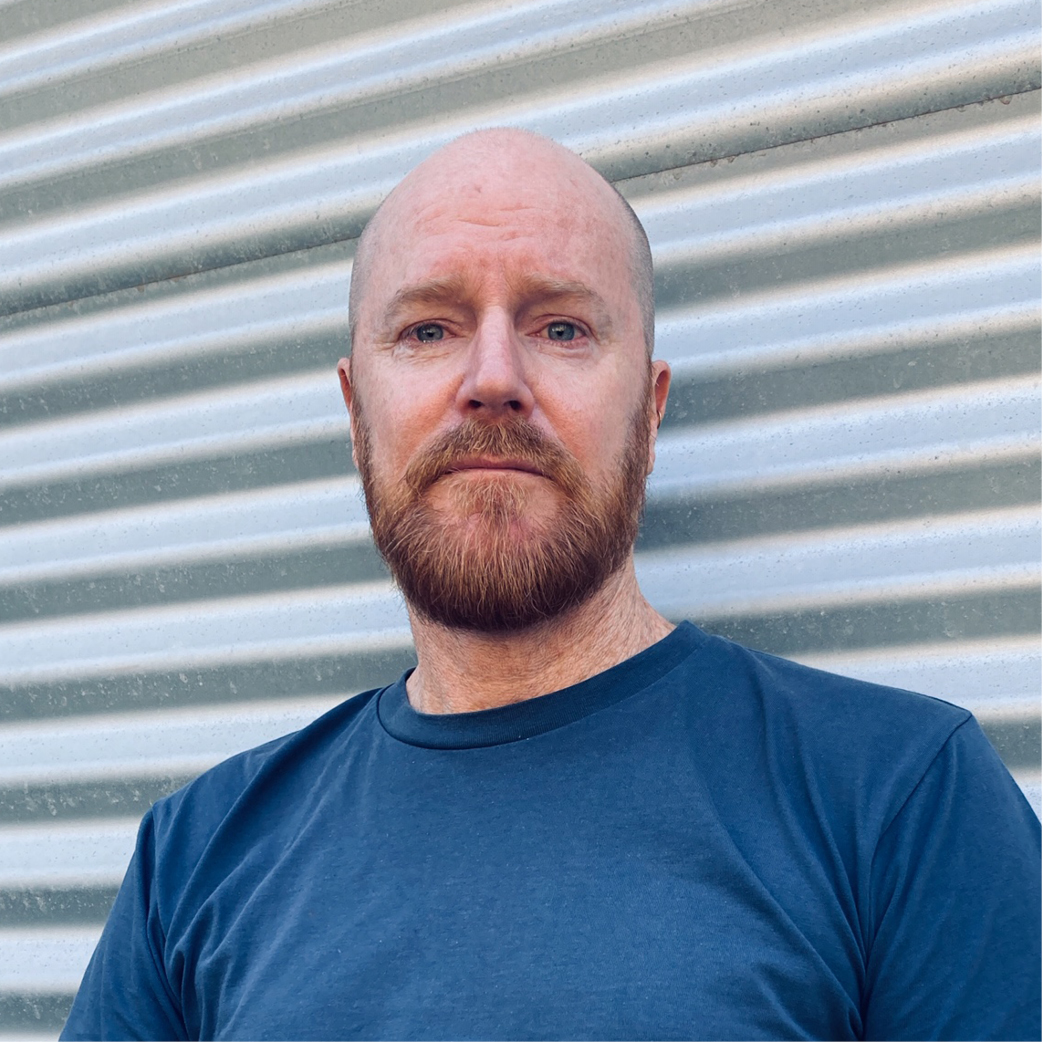 Image of a man in a blue shirt leaning on a grey garage door.