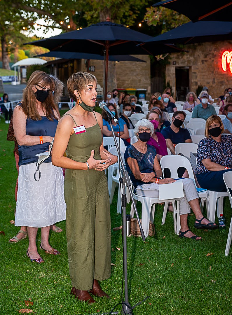 A woman stands in front of a microphone with the audience standing behind her.